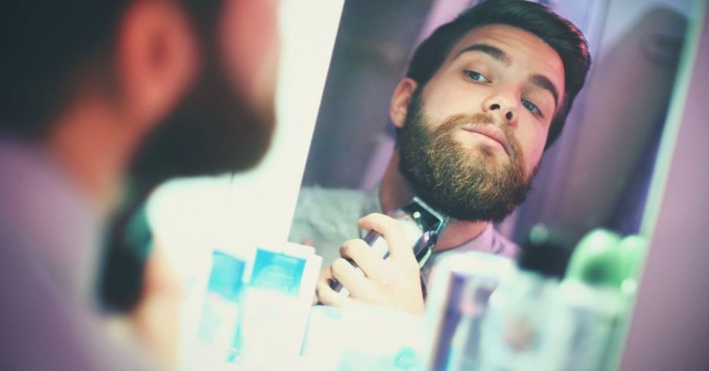 Man trimming his beard in front of a mirror